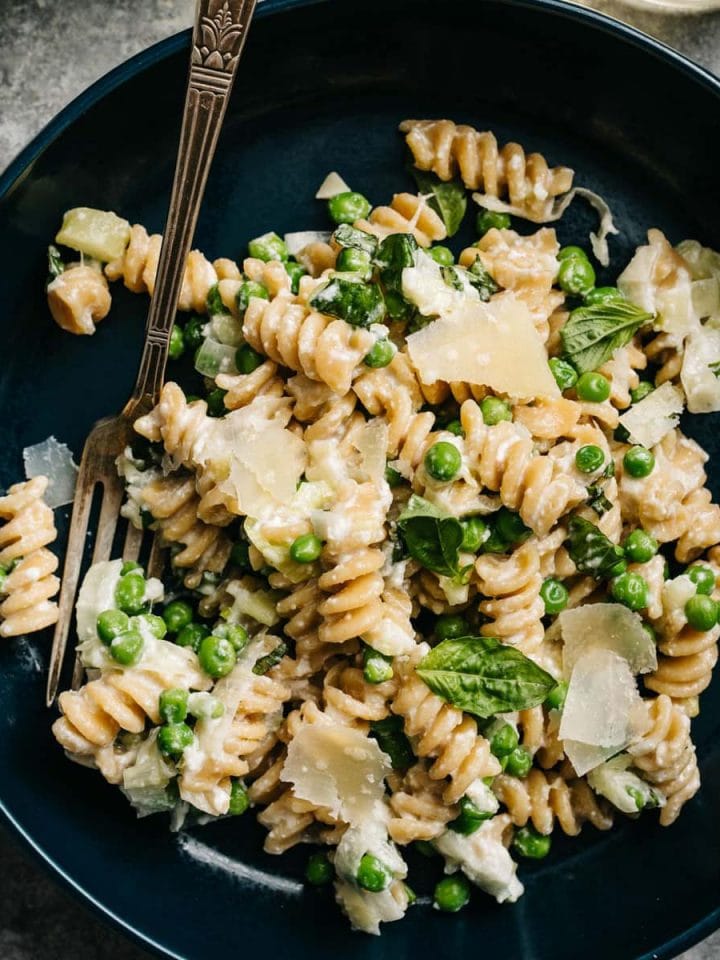 Easy weeknight ricotta pasta with peas in a blue bowl with a side of parmesan cheese.
