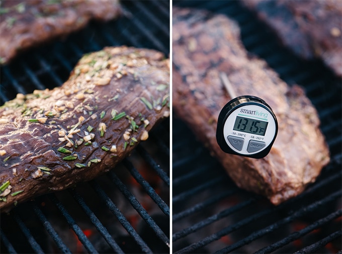 Rosemary marinated flank steak on a grill with an instant read thermometer showing a temperature of 130.