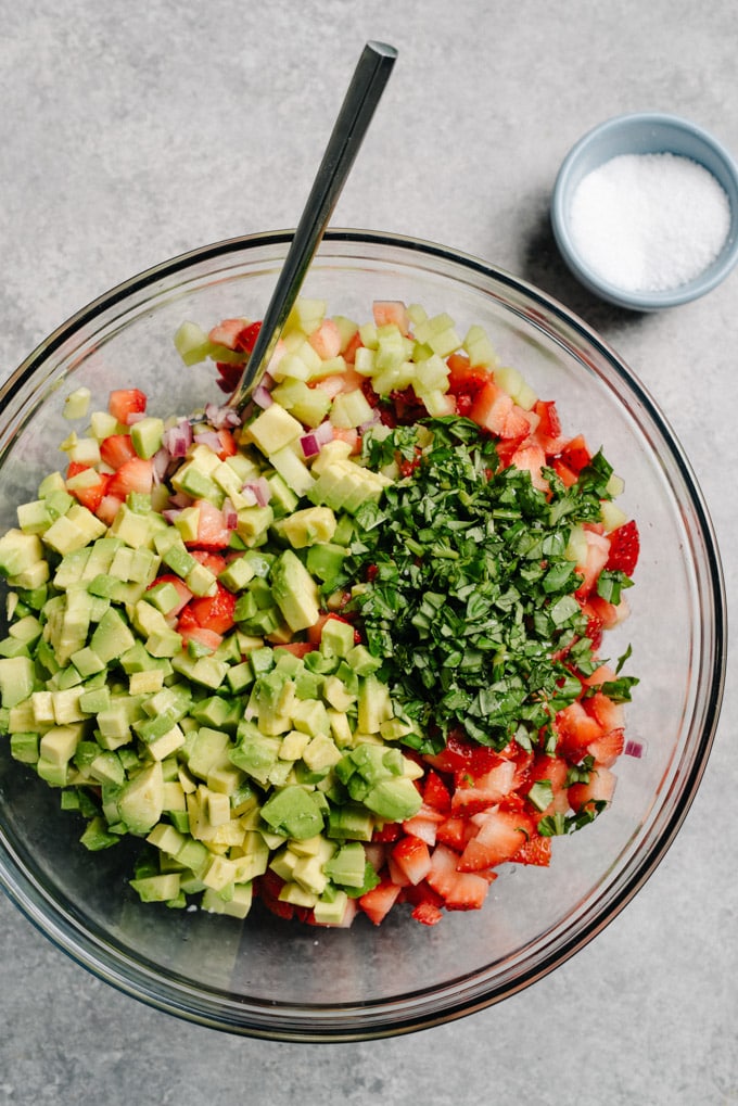 A glass bowl filled with the prepped ingredients for vegan strawberry avocado salsa.