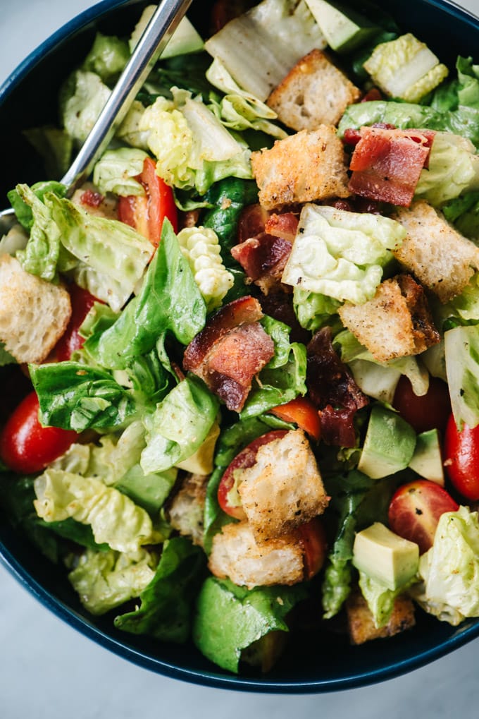 From above, a close-up of a BLT salad with avocado and hot bacon dressing.