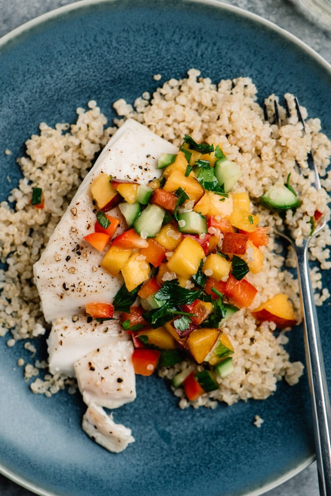 Oven baked halibut fish over quinoa topped with fresh peach salsa on a blue plate. 