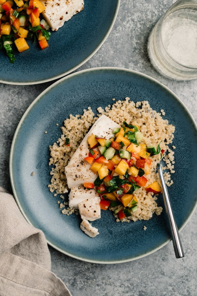 Oven baked halibut fish over quinoa topped with fresh peach salsa on a blue plate.