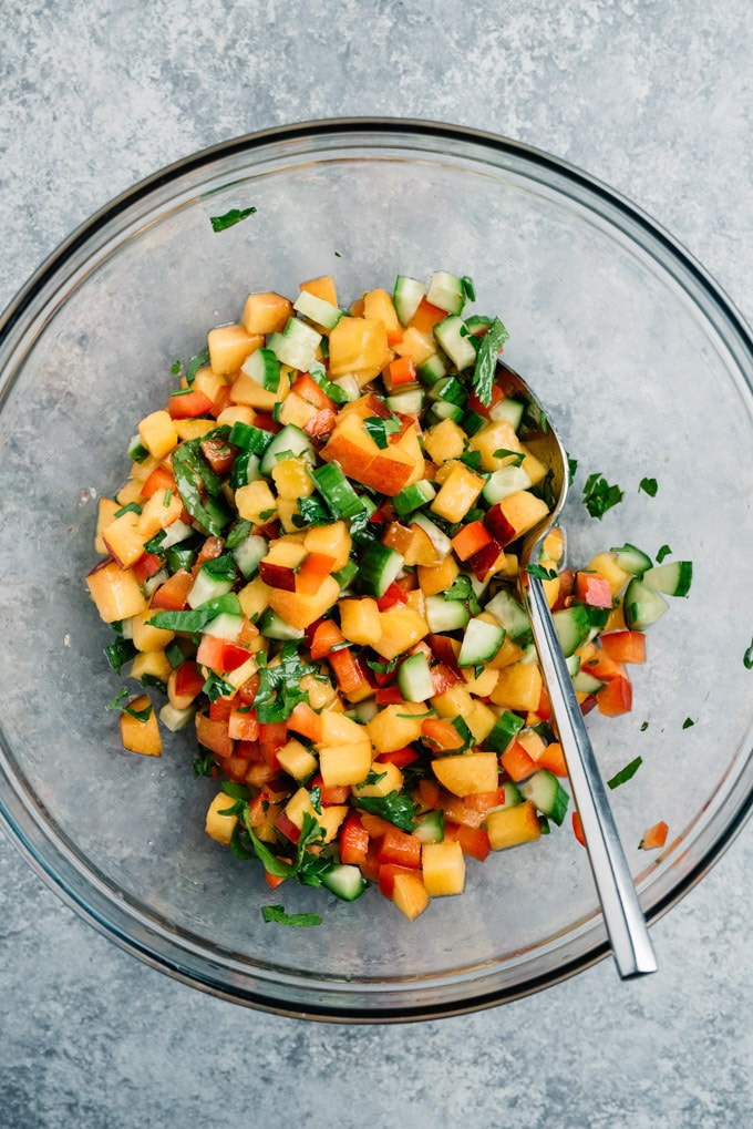 Peach salsa in a mixing bowl made with fresh diced peaches, persian cucumbers, red bell pepper, parsley, lime juice, salt, and pepper.