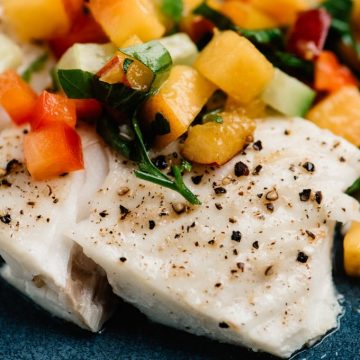 Side view, baked halibut fillet topped with fresh peach salsa.