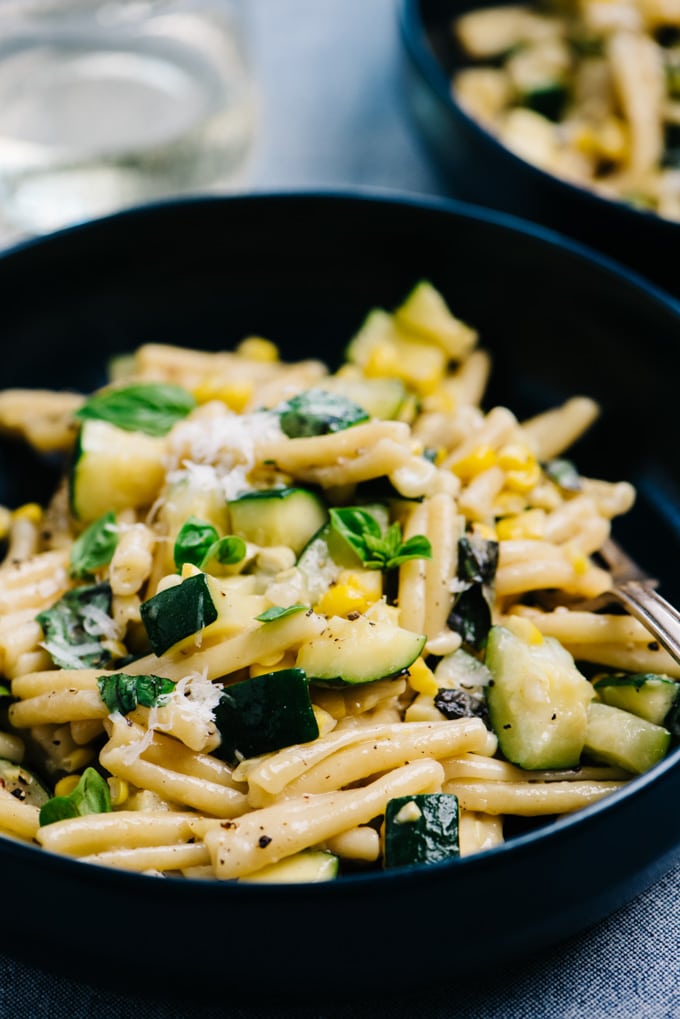 Side view of a bowl of summer pasta with zucchini and sweet corn.