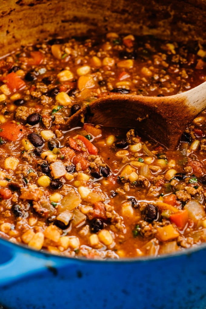 Side view, a wood spoon tucked into a pot of ground beef taco soup with black beans.