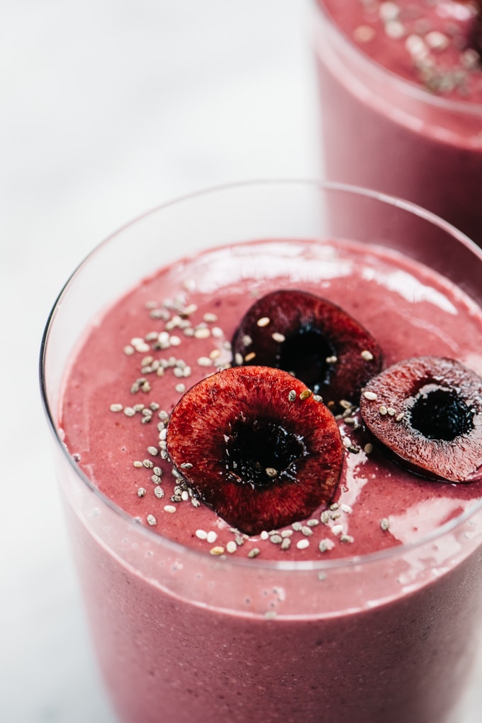 Side view, a close-up of a cherry smoothie in a glass garnished with fresh cherries and chia seeds.
