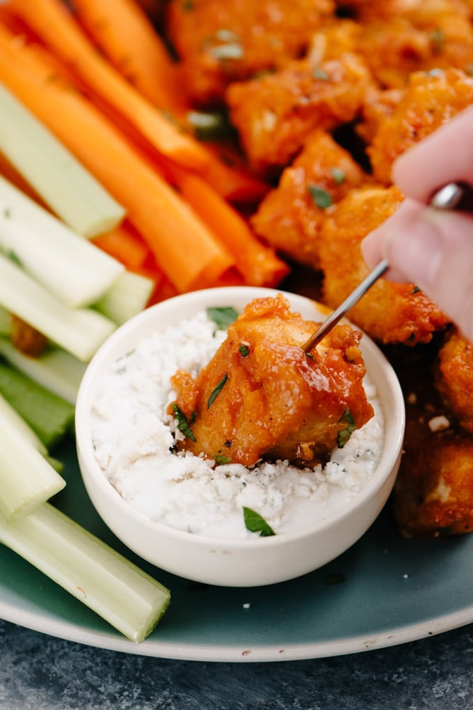 A buffalo chicken bite on a cocktail stick being dipped into blue cheese dressing.
