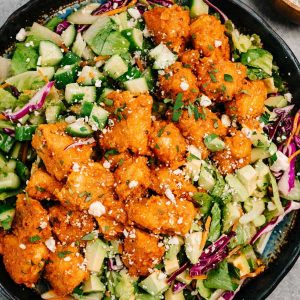 A large buffalo chicken salad arranged in a salad platter with a small side dish of blue cheese crumbles.