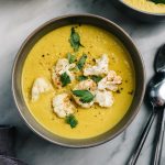 From above, two bowls of curried cauliflower soup on a marble table.