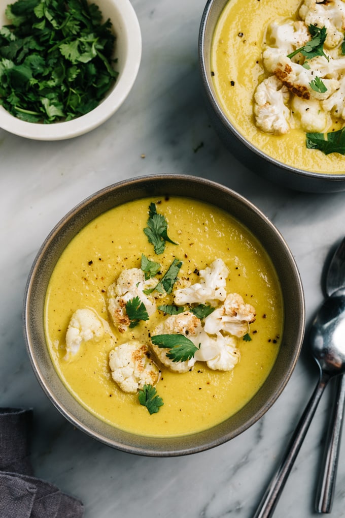 From above, two bowls of curried cauliflower soup on a marble table.