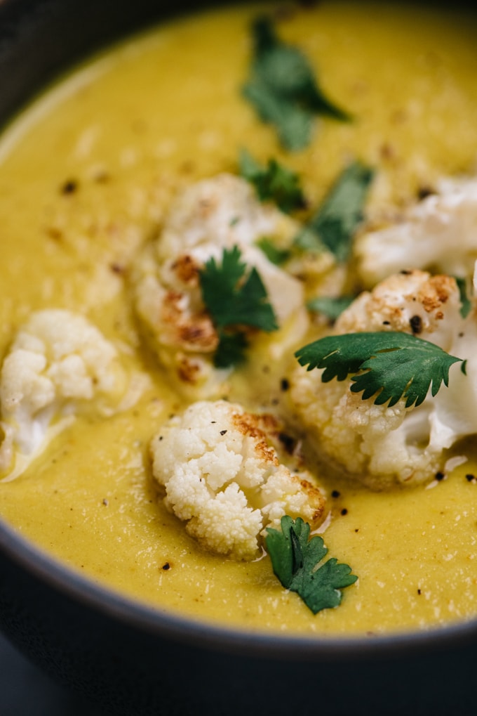 Side view of curried cauliflower soup in a grey bowl garnished with roasted cauliflower florets and fresh cilantro.