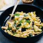 Side view of a bowl of summer pasta with zucchini and sweet corn on a blue tablecloth.