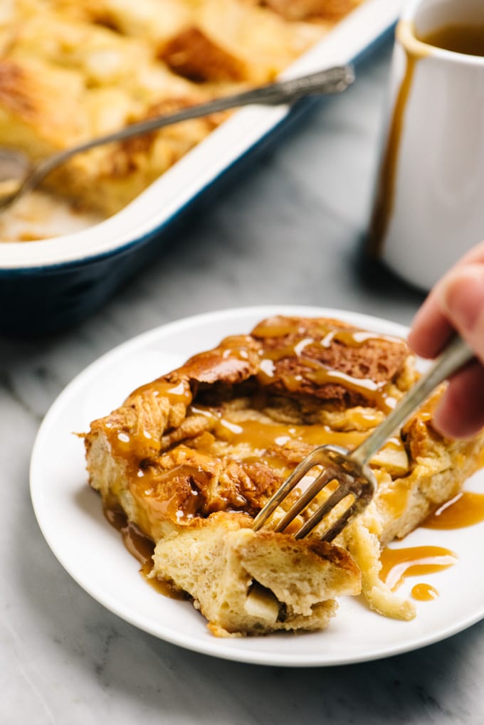 A fork inserted into a piece of apple bread pudding drizzled with salted caramel sauce.