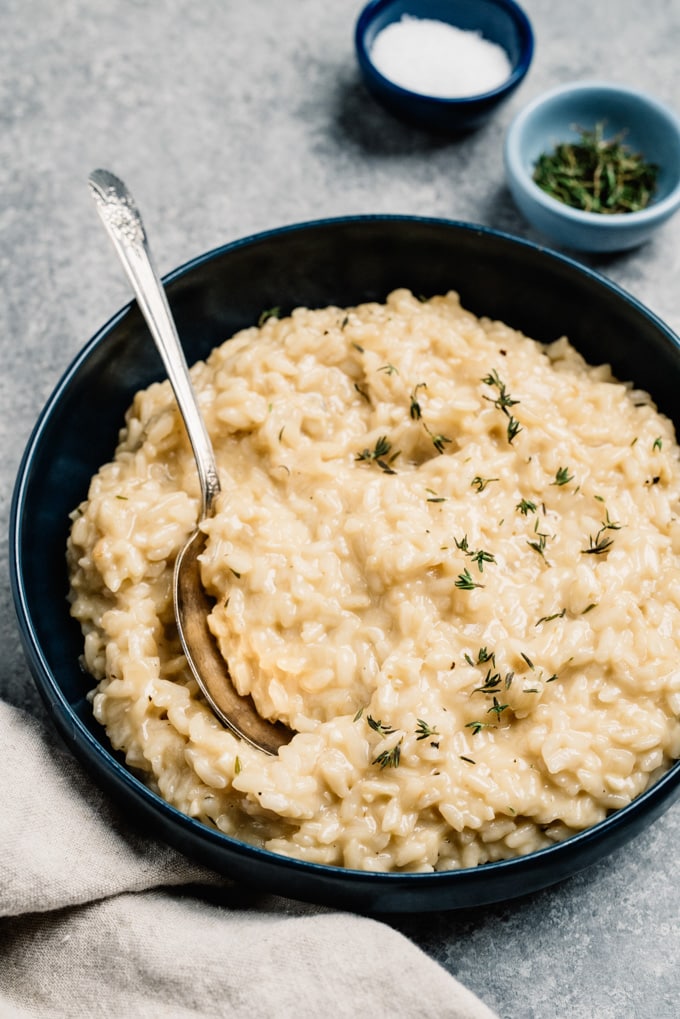 Side view, instant pot risotto in a blue serving bowl with thyme on a cement background.