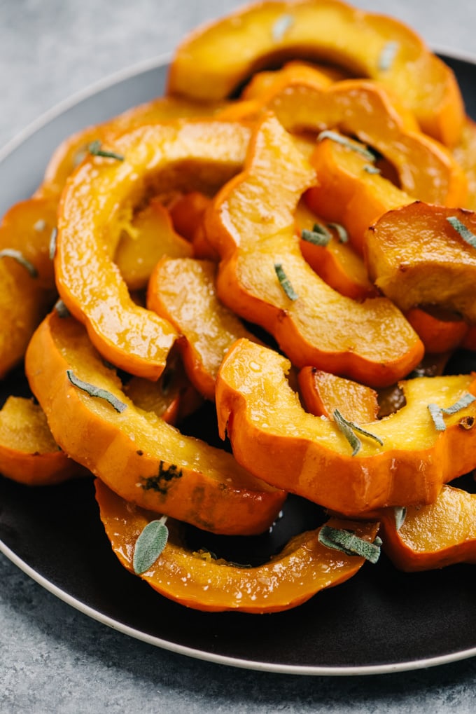 A platter of roasted acorn squash with maple brown butter garnished with fresh sage.