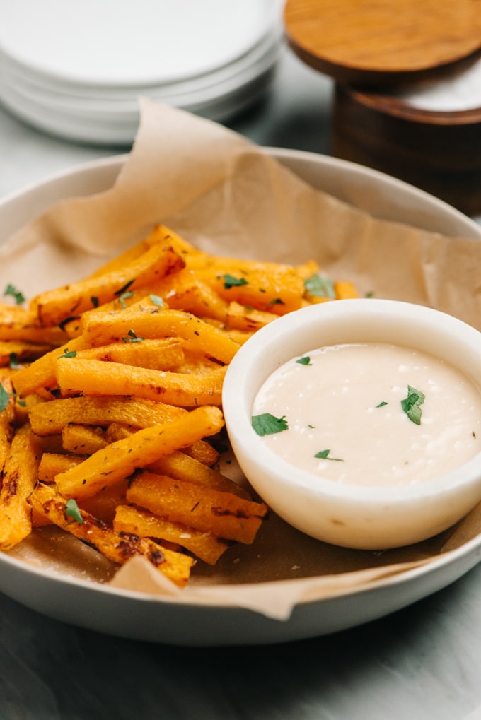 Side view of a bowl of butternut squash fries with maple aioli dipping sauce.