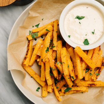 A plate of oven baked butternut squash fries with a small bowl of maple aioli dipping sauce.