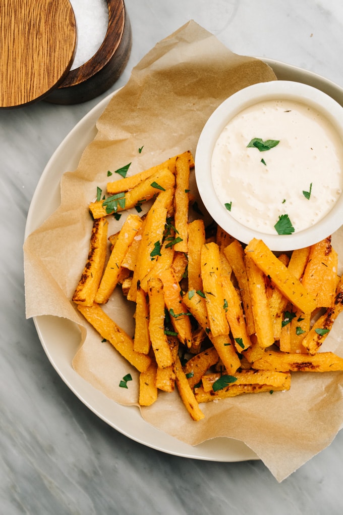 A plate of oven baked butternut squash fries with a small bowl of maple aioli dipping sauce.