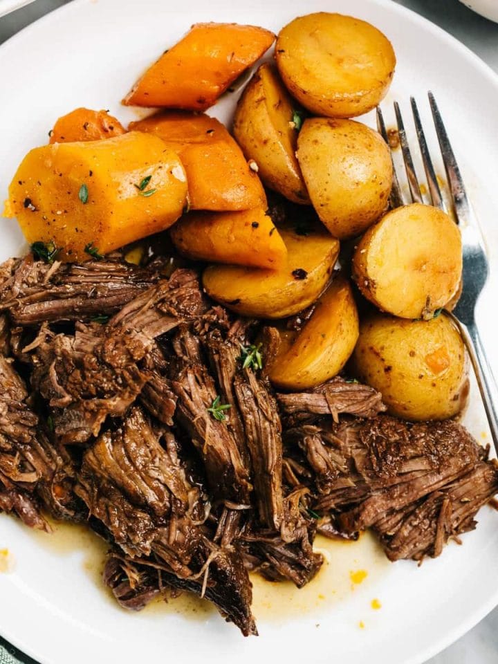A serving of instant pot pot roast on a white plate with carrots and potatoes on a marble table.