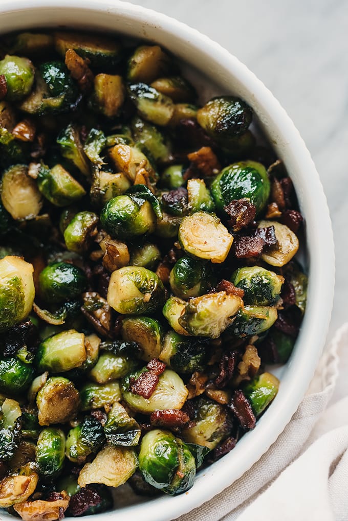 A bowl of sautéed maple bacon Brussels sprouts on a marble table.