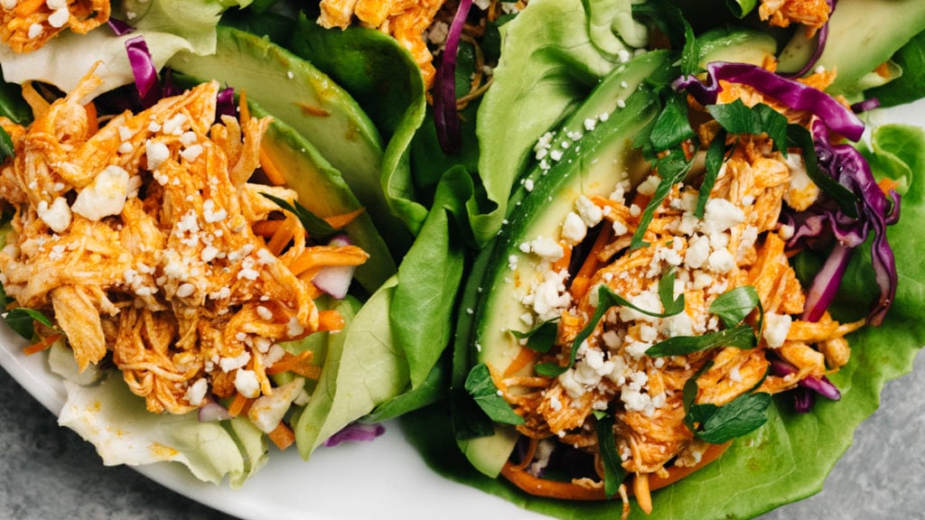 A platter of healthy buffalo chicken lettuce wraps with avocado and blue cheese crumbles.