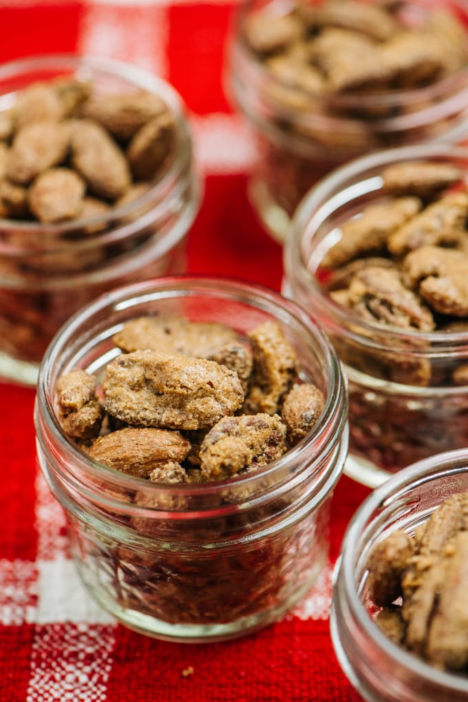 Several small gift jars of cinnamon sugar candied nuts on a red and white plaid tablecloth.