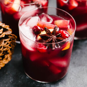 Side view, two glasses of Christmas Sangria garnished with apples, oranges, cranberries, and whole spices.