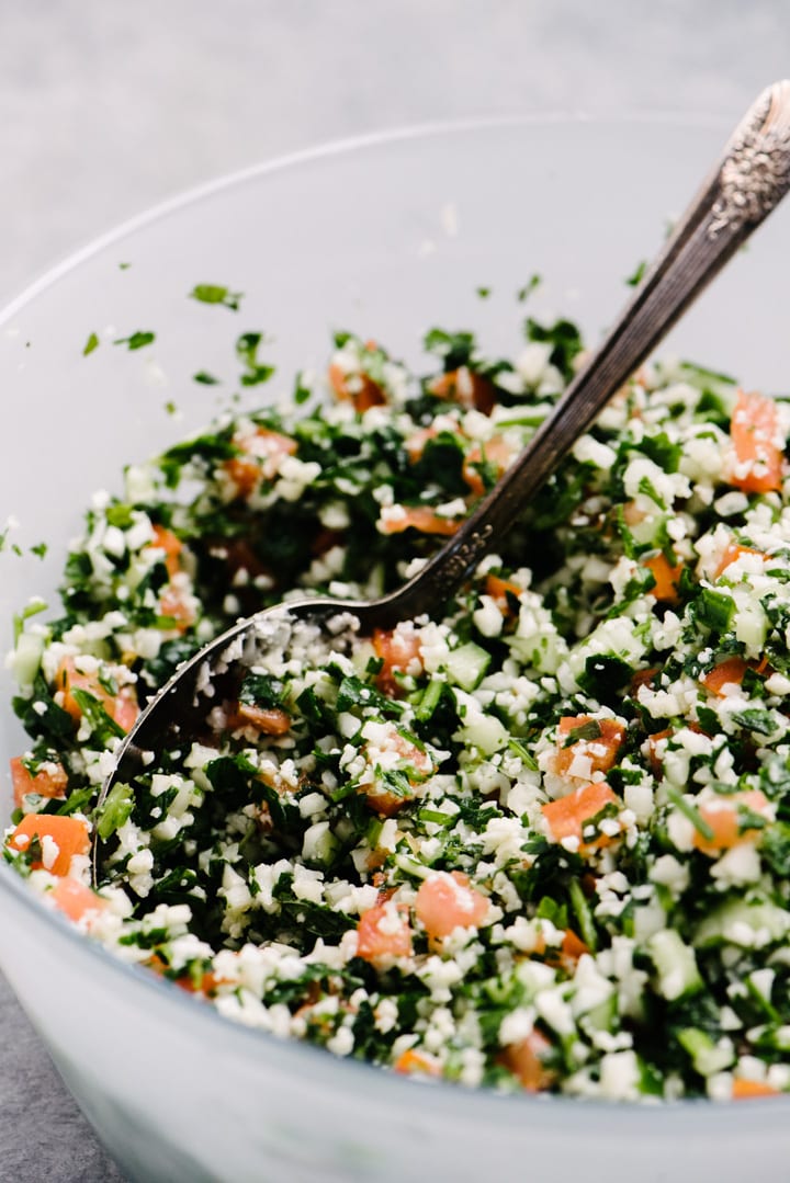 Side view, cauliflower tabbouleh in a glass frosted bowl with a vintage serving spoon.