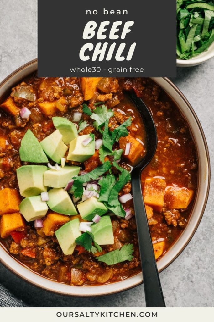 A black spoon tucked into a bowl of no bean beef chili with sweet potatoes, topped with avocado, cilantro and diced red onions; title bar at the top reads "no bean beef chili; whole30 and grain free".