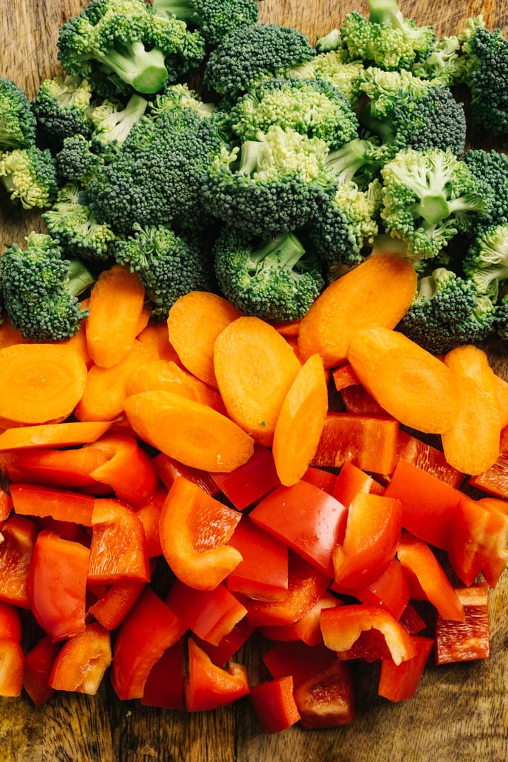 Chopped broccoli, carrots, and bell peppers on a cutting board.