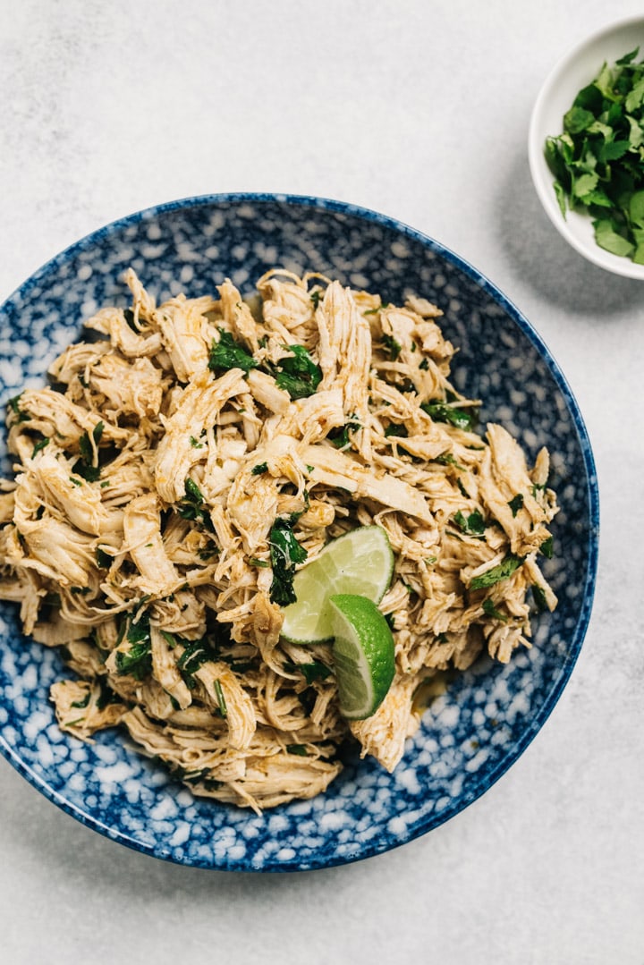 Shredded cilantro lime chicken cooked in the instant pot in a blue patterned bowl.