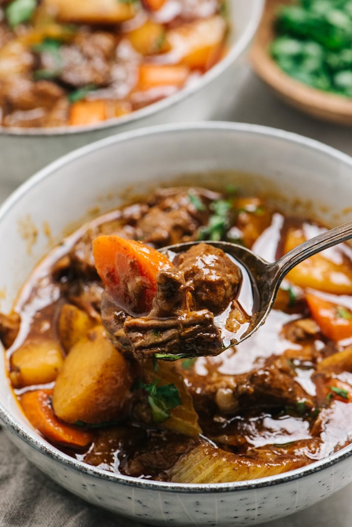 A spoonful of easy dutch oven beef stew hovering over a bowl.