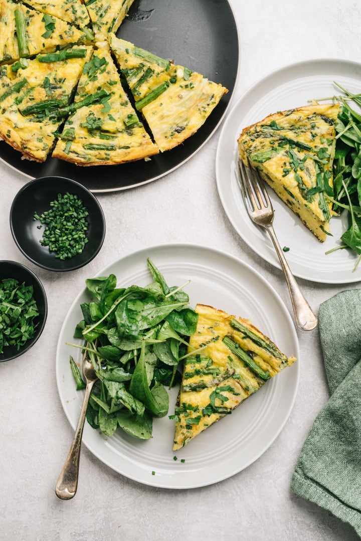 Two slices of asparagus frittata with an arugula side salad on a dining table. 