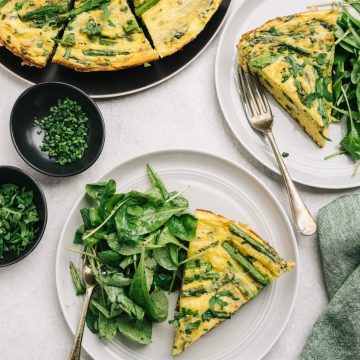 Two slices of asparagus frittata with an arugula side salad on a dining table.