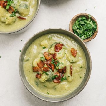 Two bowls of creamy broccoli potato soup garnished with bacon.