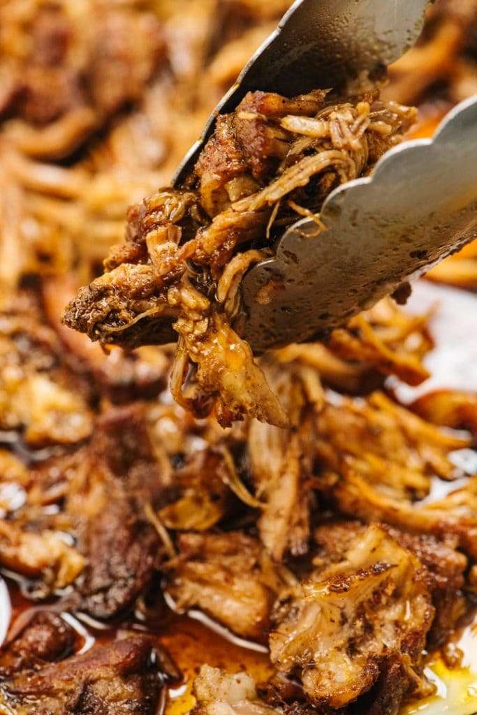 Tongs holding a serving of pulled pork cooked in the instant pot.