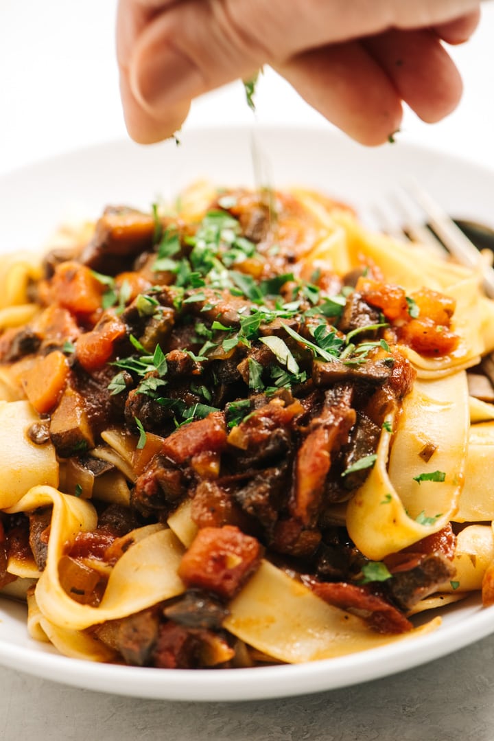 Garnishing a bowl of mushroom bolognese over pappardelle noodles with fresh chopped parsley.