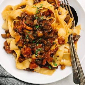 Mushroom bolognese with pasta served in a bowl with a spoon and fork
