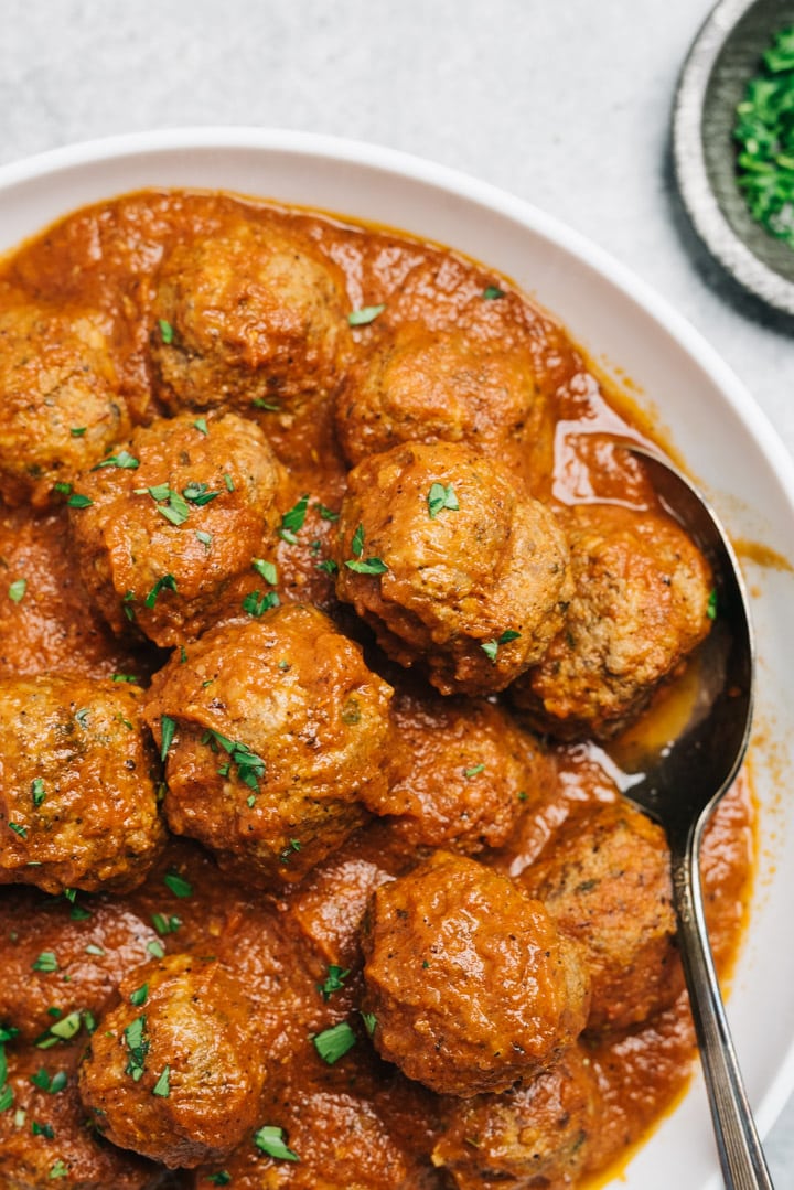 A spoon tucked into a bowl of healthy meatballs tossed with marinara sauce.