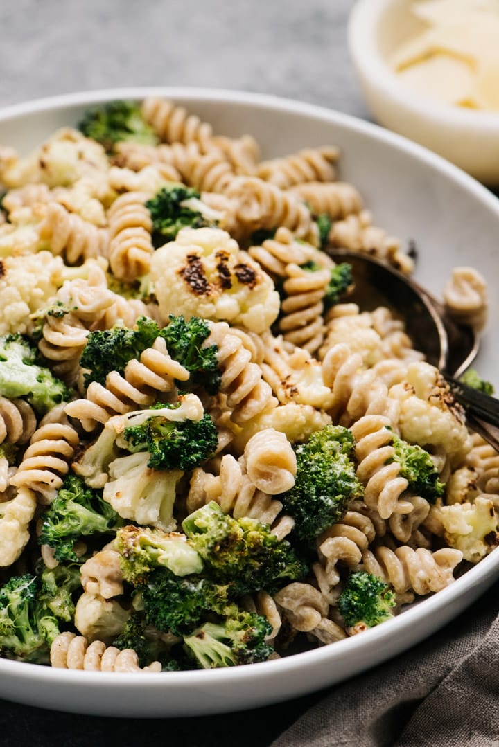 Side view, a large serving bowl of creamy pasta tossed with roasted vegetables.