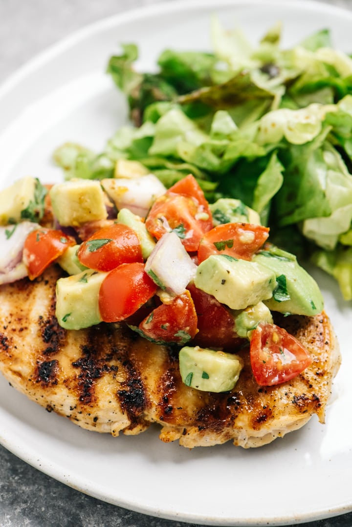 Side view, a dinner plate of grilled chicken with avocado salsa and a side salad.