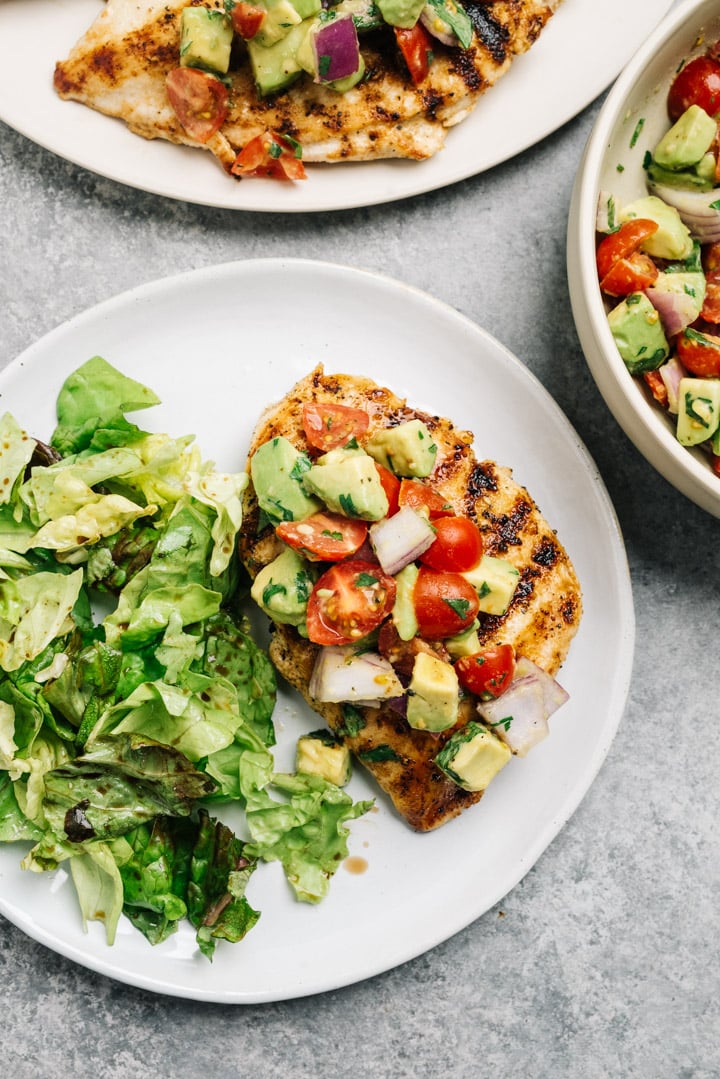 Grilled chicken breast topped with avocado salsa served with a tossed salad on a dinner table.