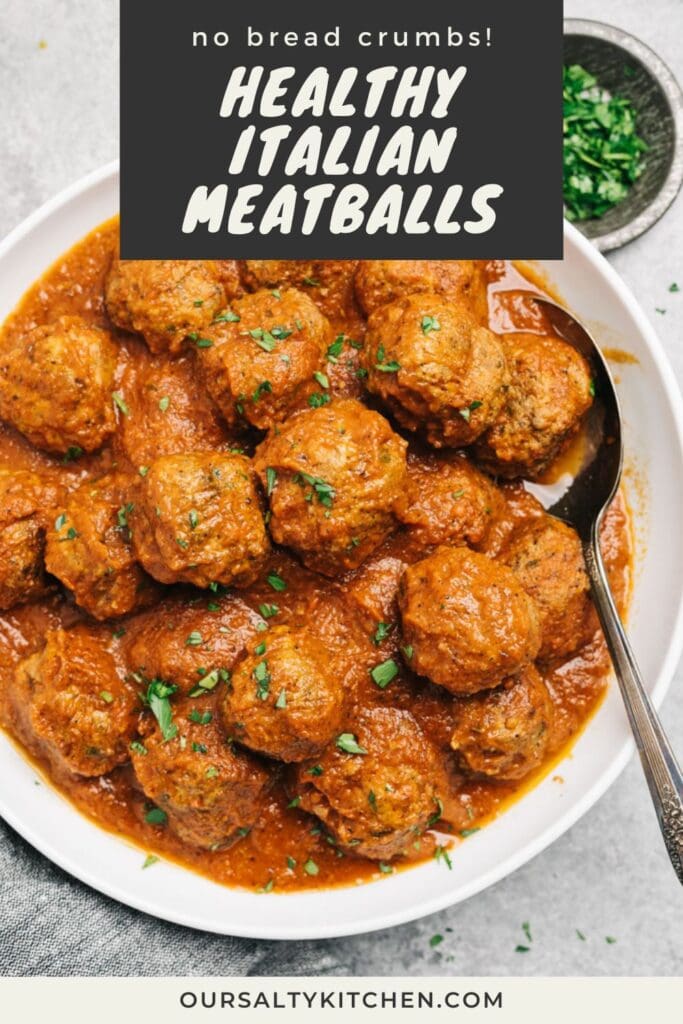 A bowl of healthy Italian-style meatballs tossed in marinara sauce on a cement background, with a bowl of fresh chopped parsley to the side.