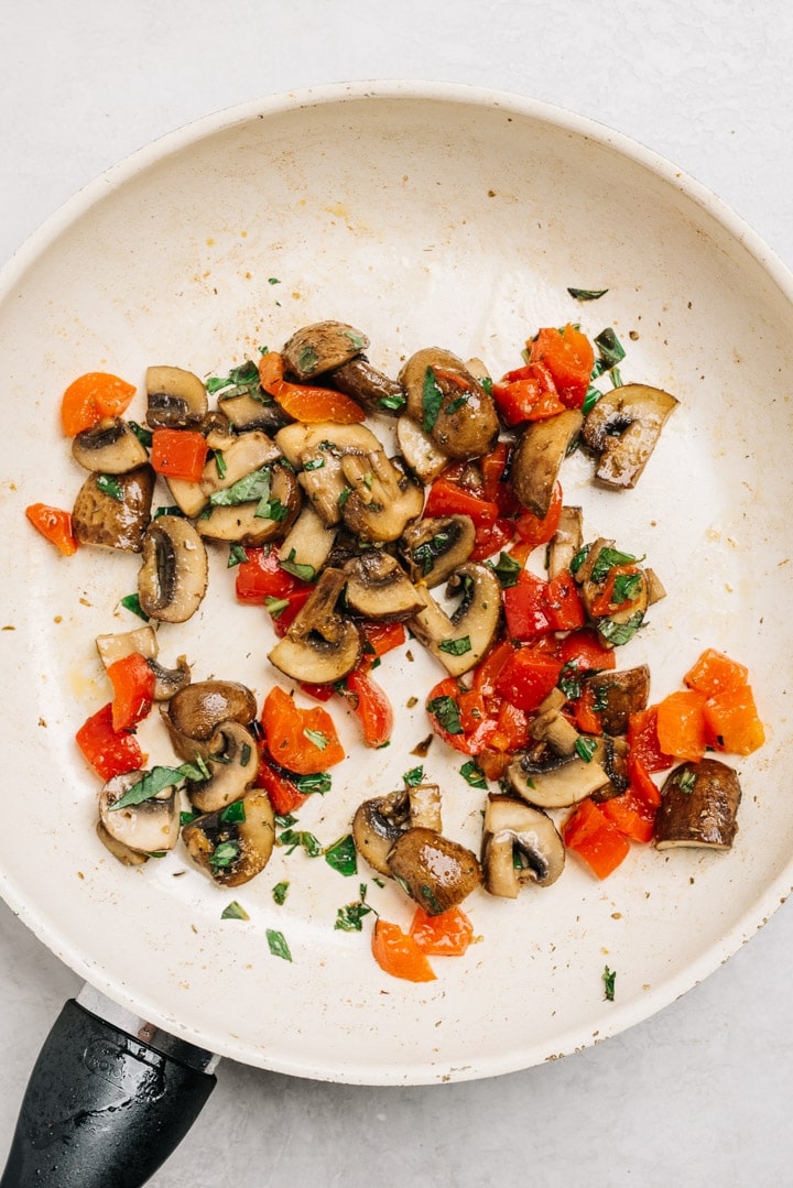 Sauteed mushrooms, roasted red peppers, and seasoning in a skillet.