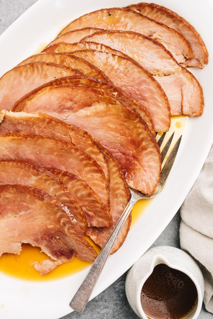 Slices of spiral ham on a white platter drizzled with maple orange glaze.