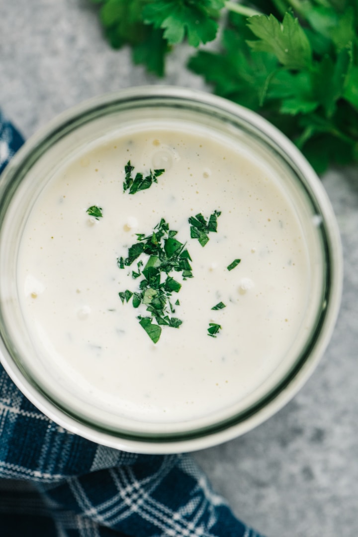 A jar of homemade Whole30 ranch garnished with fresh chopped parsley.