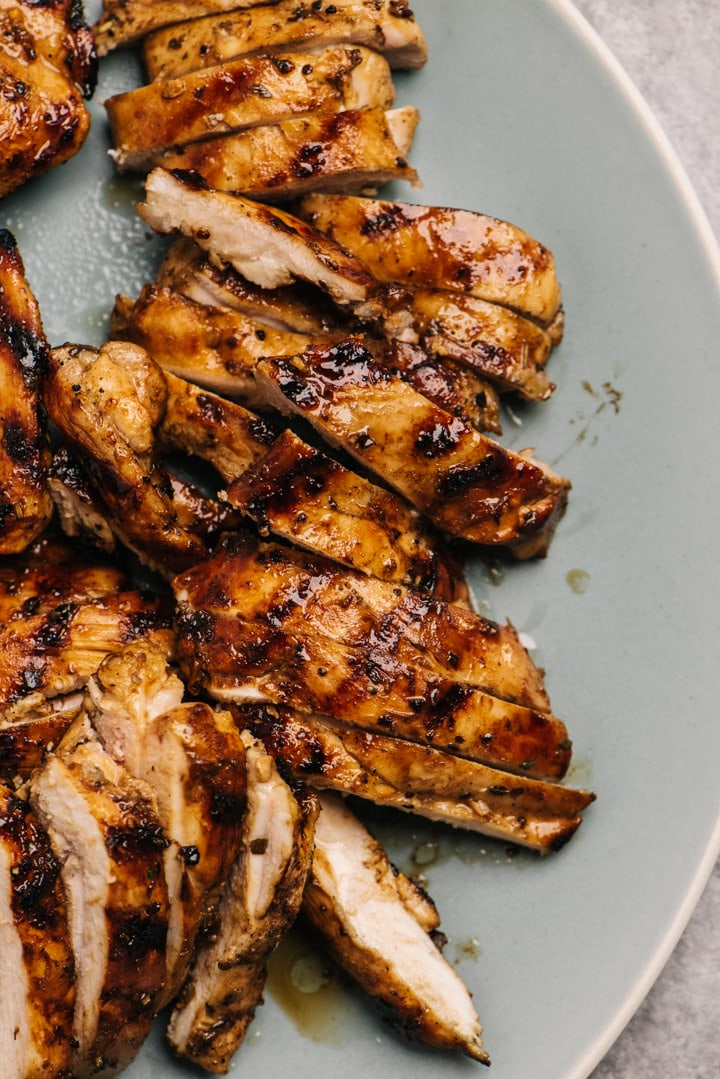 Slices of grilled balsamic chicken thighs on a blue platter.