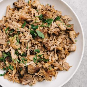 A white serving bowl of instant pot carnitas garnished with chopped cilantro.