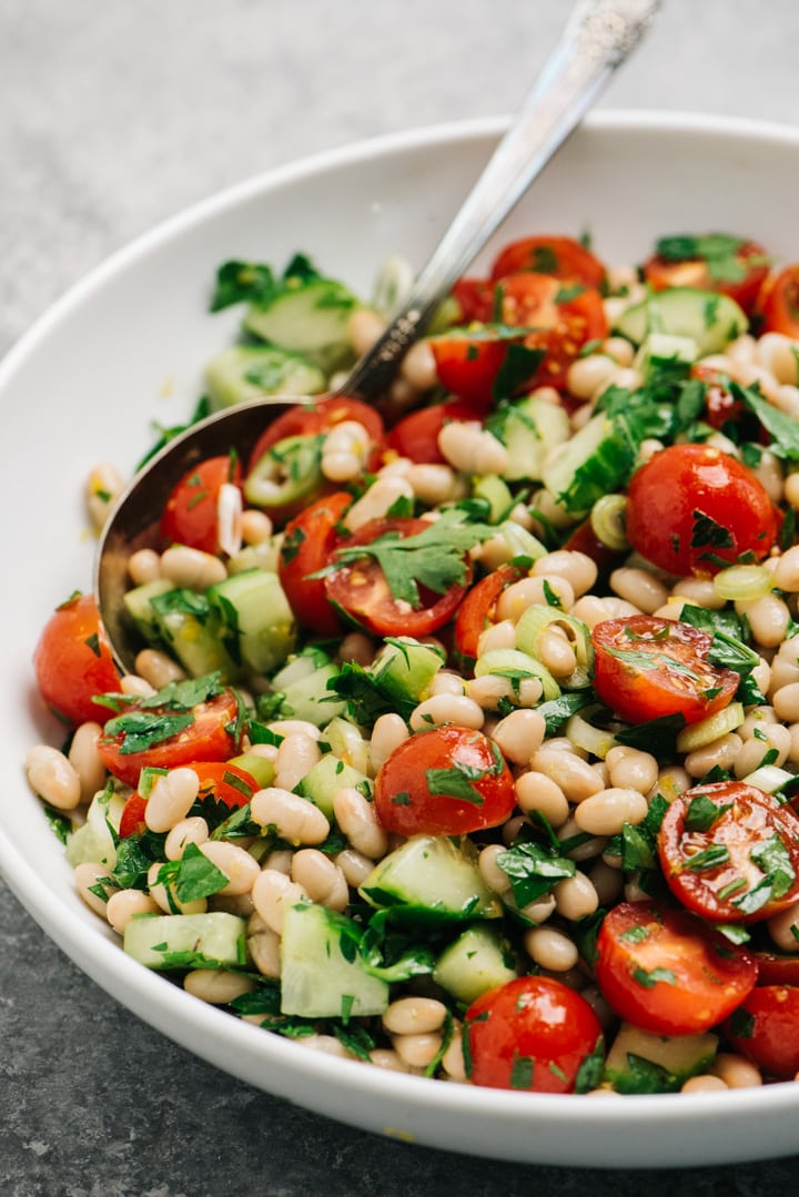 Side view, white bean salad with tomato, cucumber, and parsley in a large serving bowl.